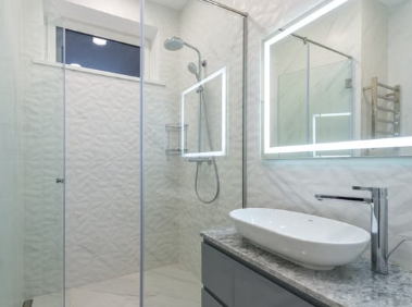 Glass walk-in shower with vessel sink and illuminated mirror
